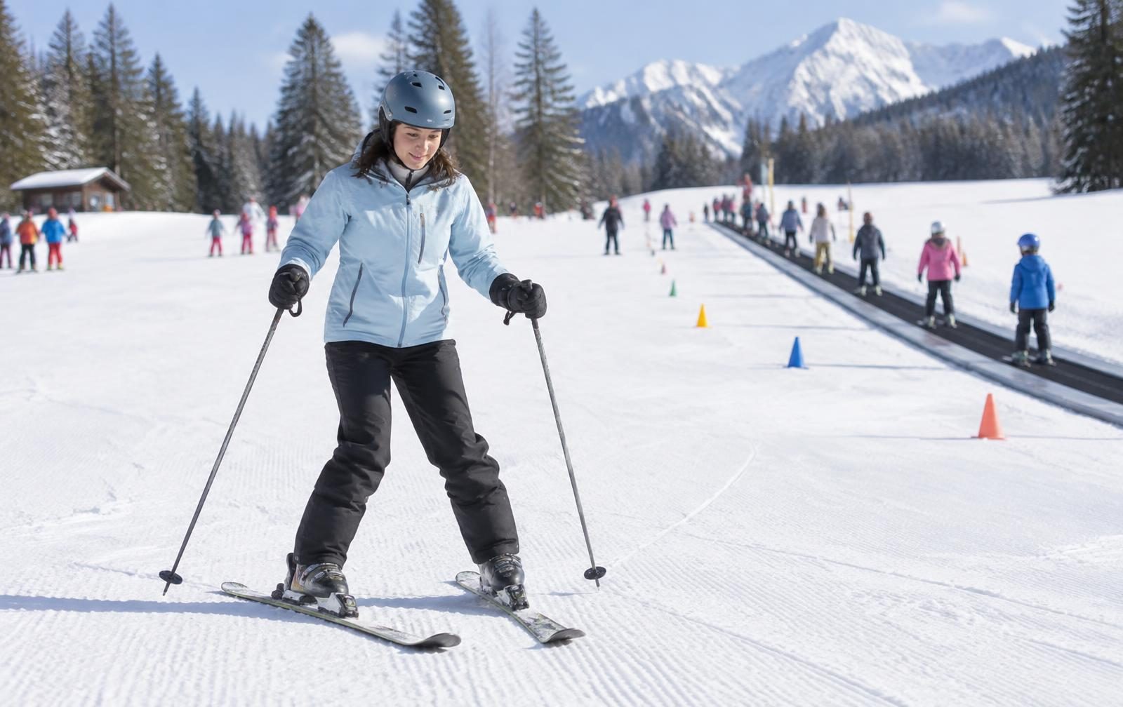 A new skier making a slow turn on a gentle beginner slope beside a ski school area