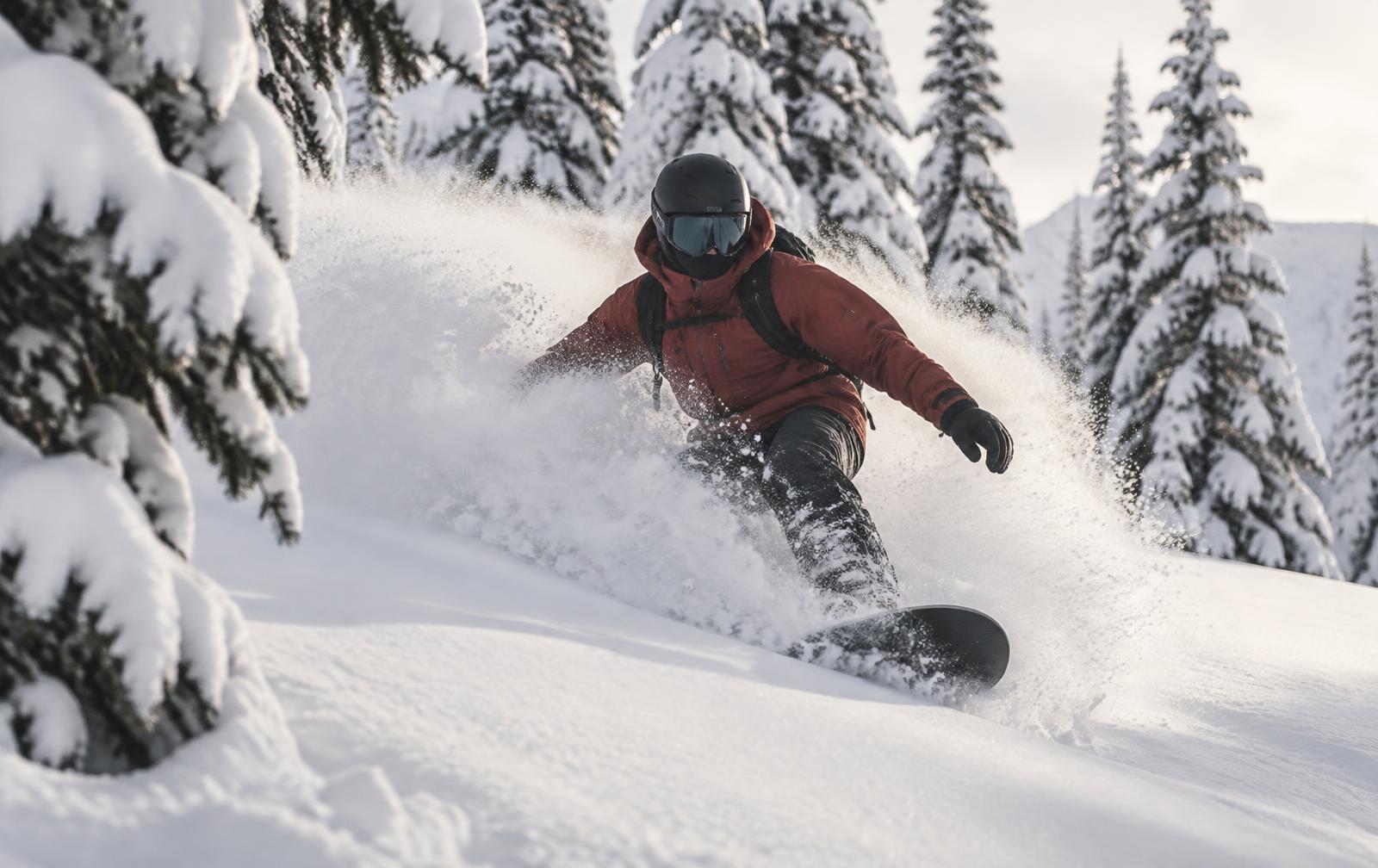 A snowboarder in a red jacket spraying deep powder snow between snow-laden pine trees