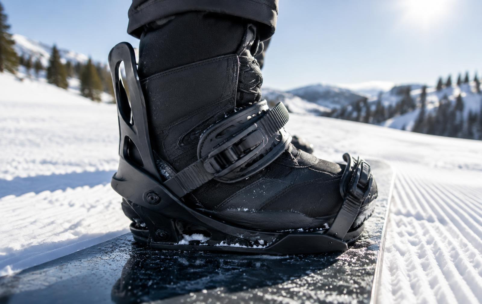 Close-up of a black snowboard boot strapped into a binding on a groomed slope